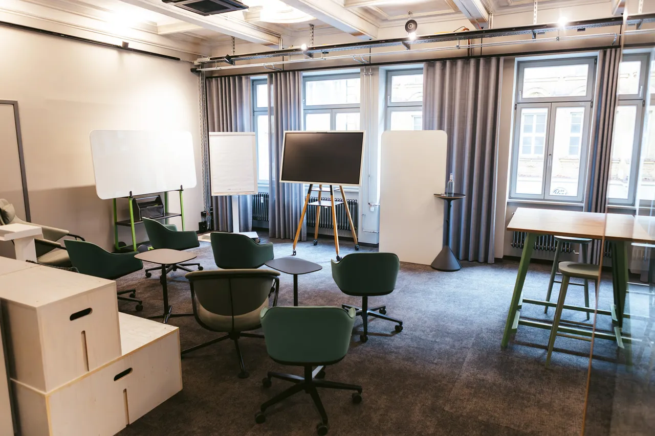 Studio im club199 mit Sesselkreis, Whiteboard und Stehtischen bei Tageslicht